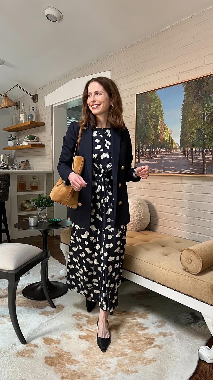 A woman wearing a navy floral dress and a dark blazer standing in a room.