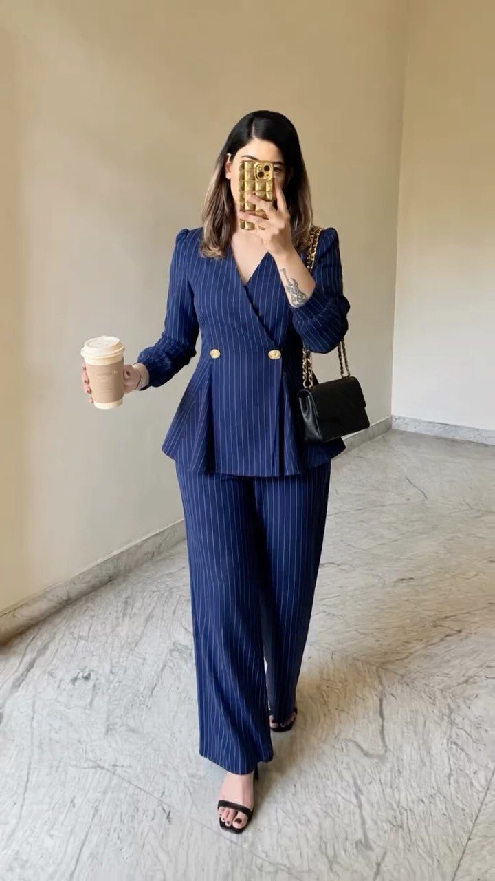 Woman wearing a navy blue pinstriped blazer and matching wide-leg trousers holding a coffee cup.