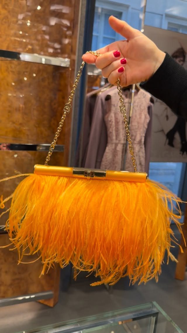 A hand holding a vibrant yellow feather clutch bag with a gold chain strap.