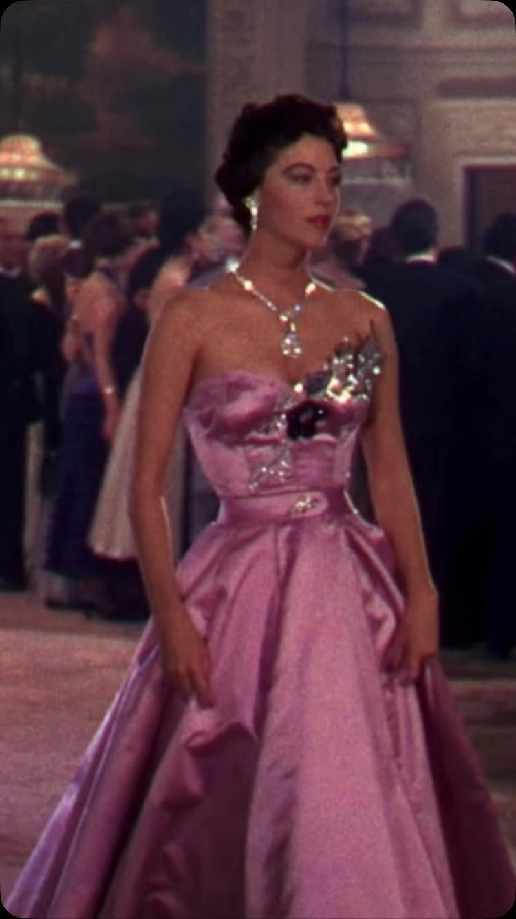 A woman wearing a vintage pink strapless ball gown and diamond necklace in a ballroom.
