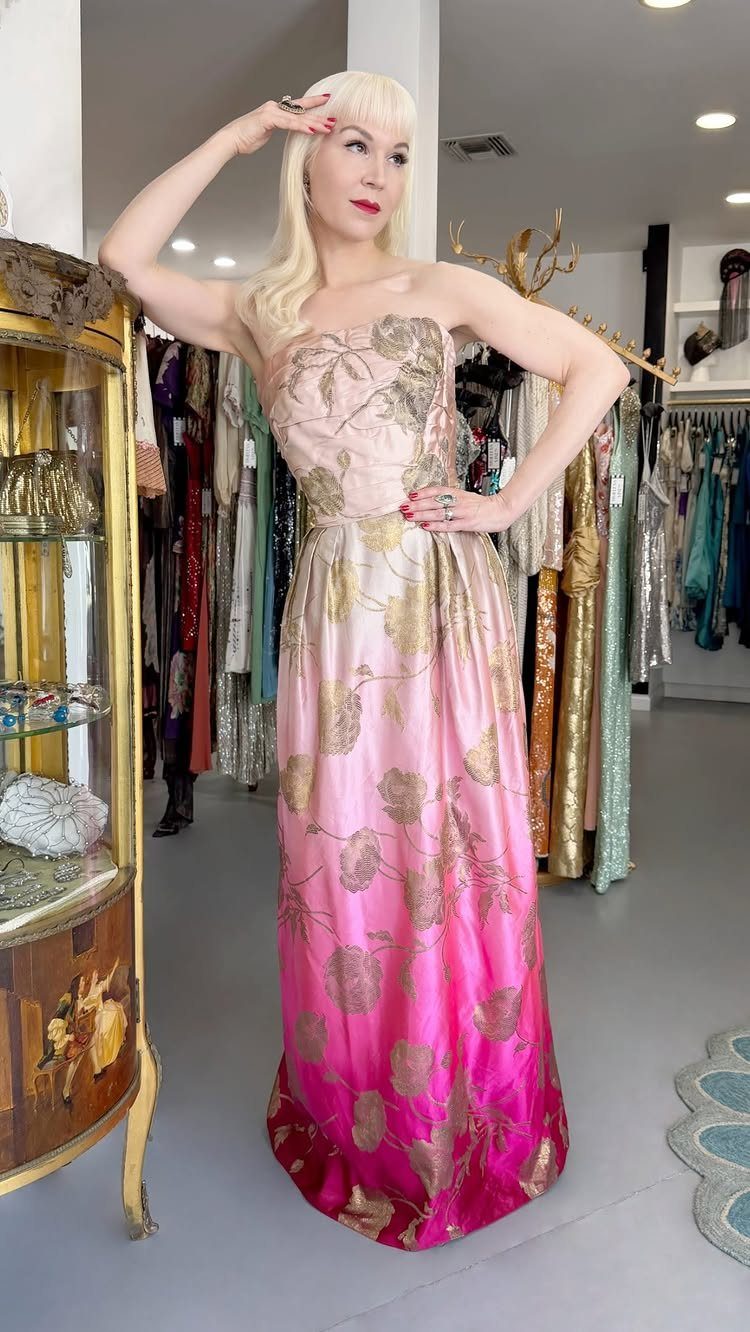 A blonde woman posing in a pink and gold floral patterned strapless gown.