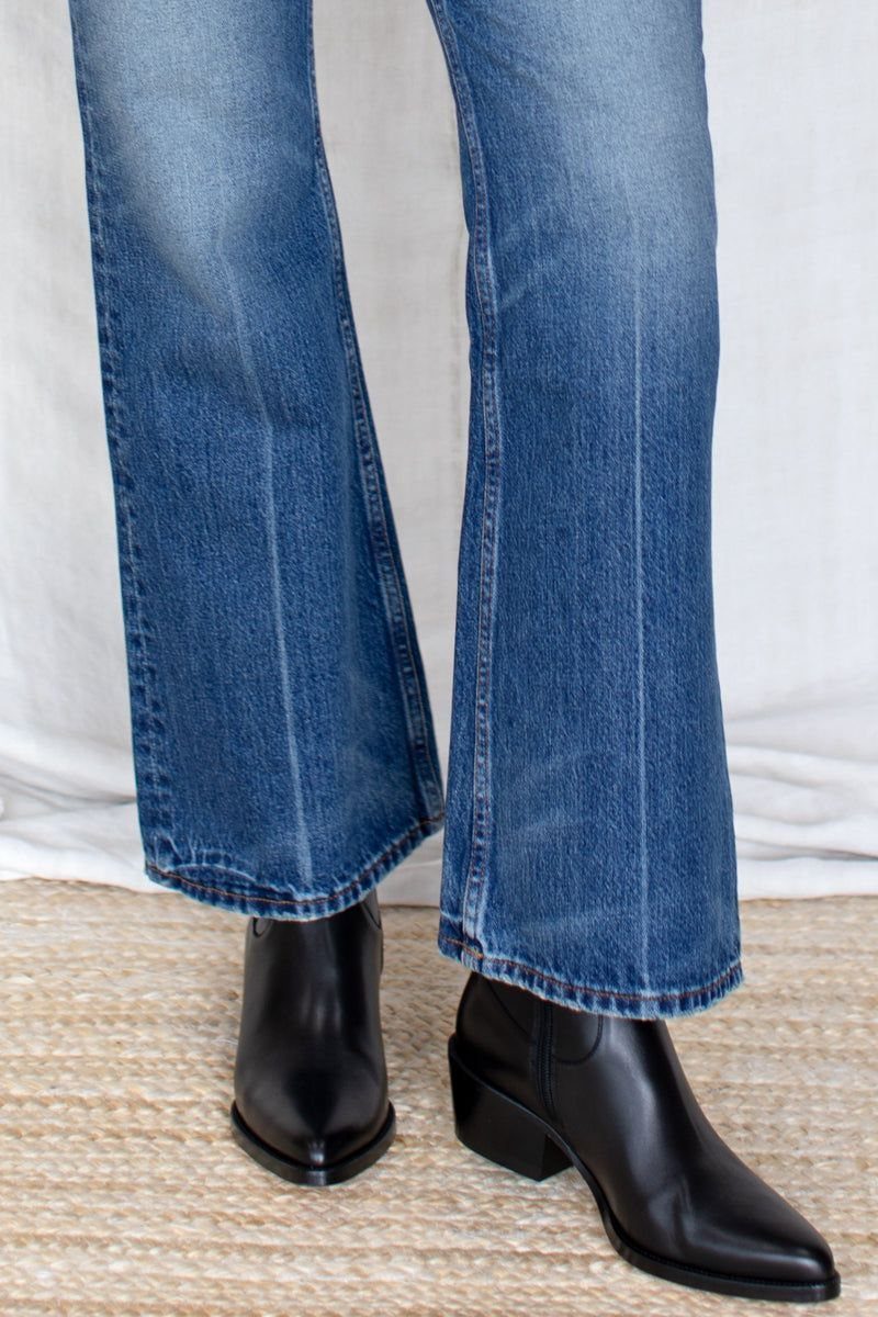 Black leather ankle boots worn with blue flared denim jeans on a woven rug.