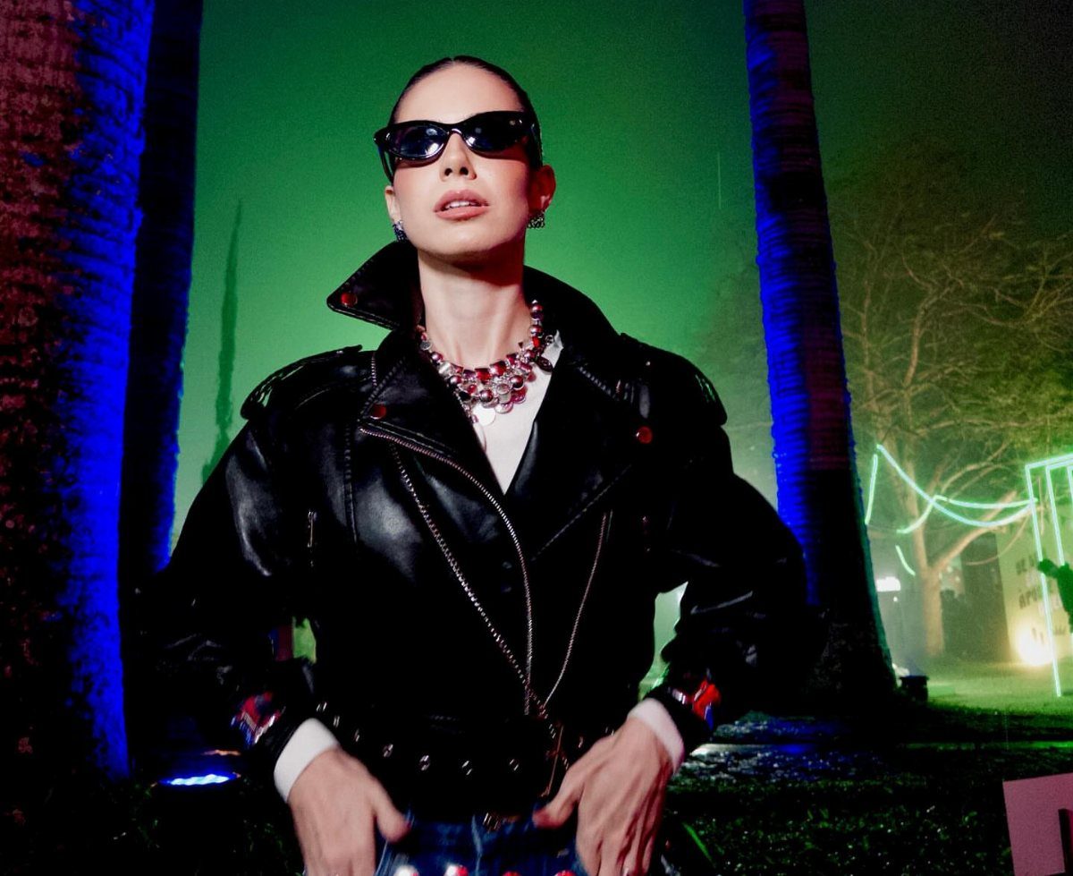 Woman wearing a black leather jacket and a large sparkling statement necklace against green light.