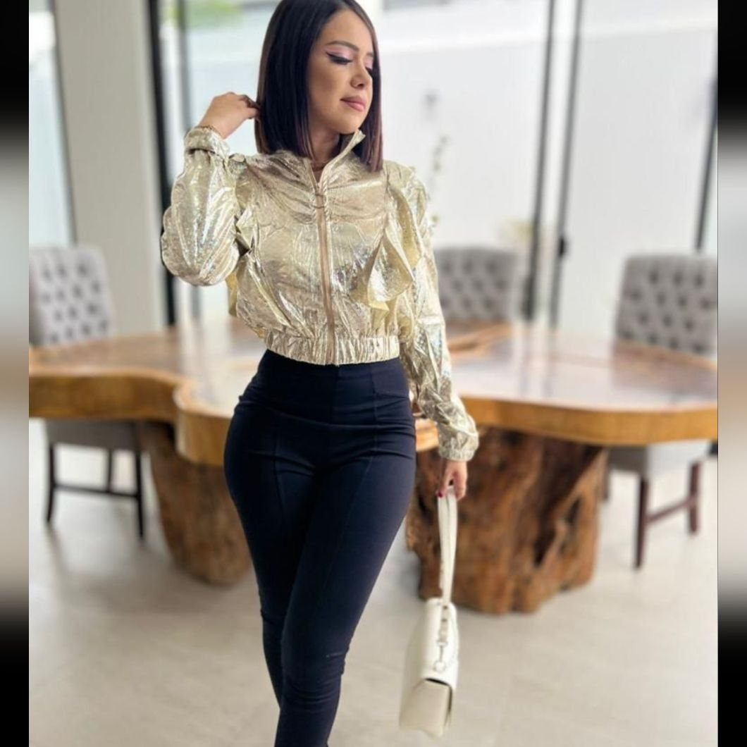 Woman wearing a shiny gold metallic cropped jacket and black high-waisted trousers.