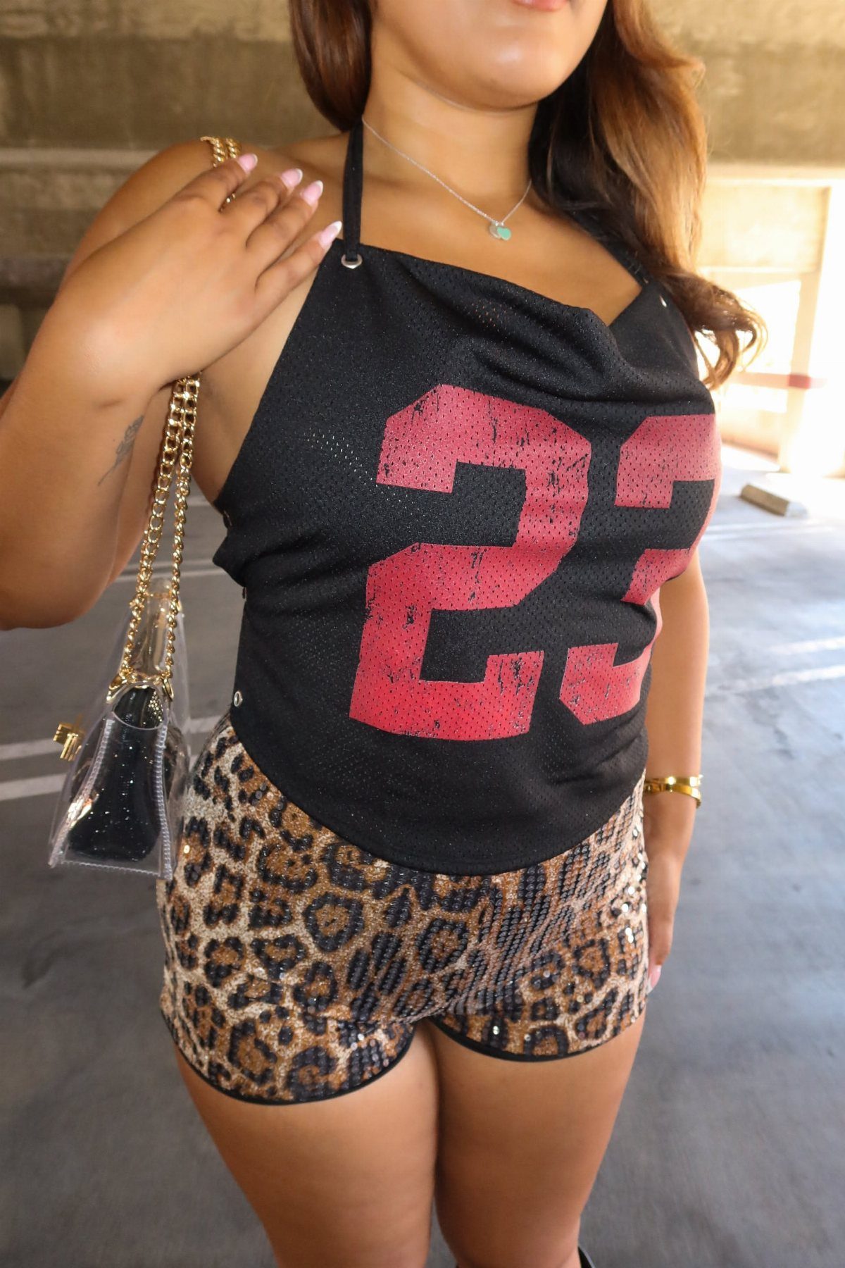 Woman wearing a black graphic halter top with red numbers and leopard print sequin shorts.