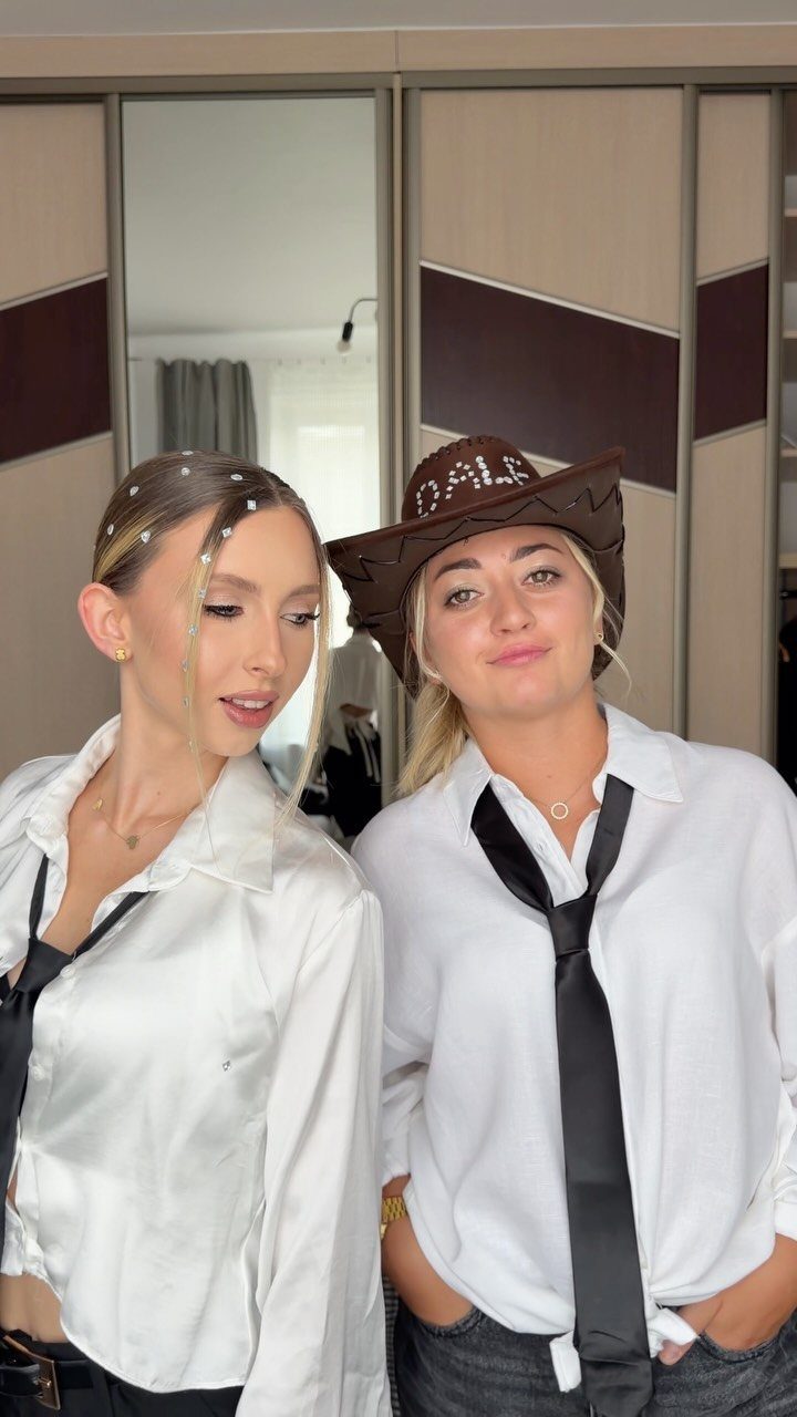 Two women wearing white button-down shirts and black ties while posing for a selfie.