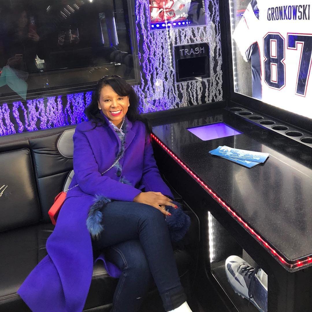 A woman in a purple coat sitting on a leather seat inside a decorated party bus.