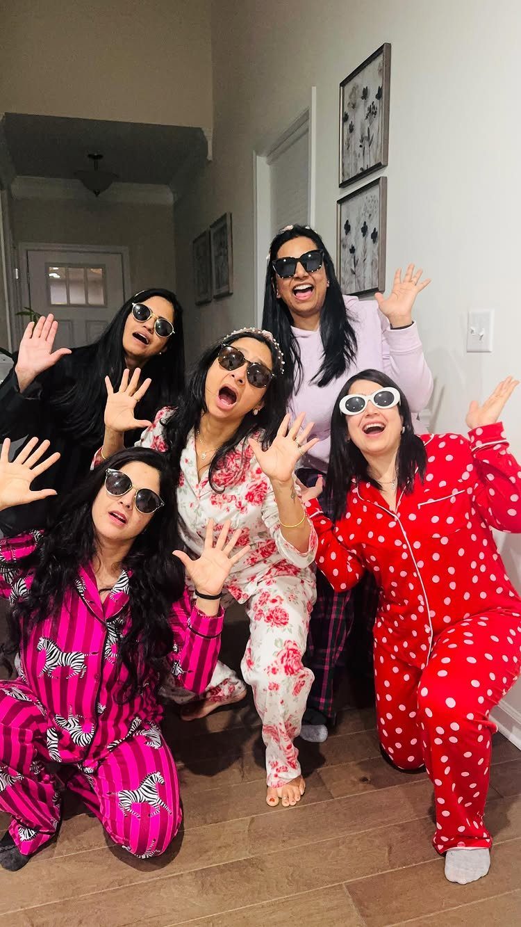 Five women in colorful patterned pajamas and sunglasses posing together in a hallway.