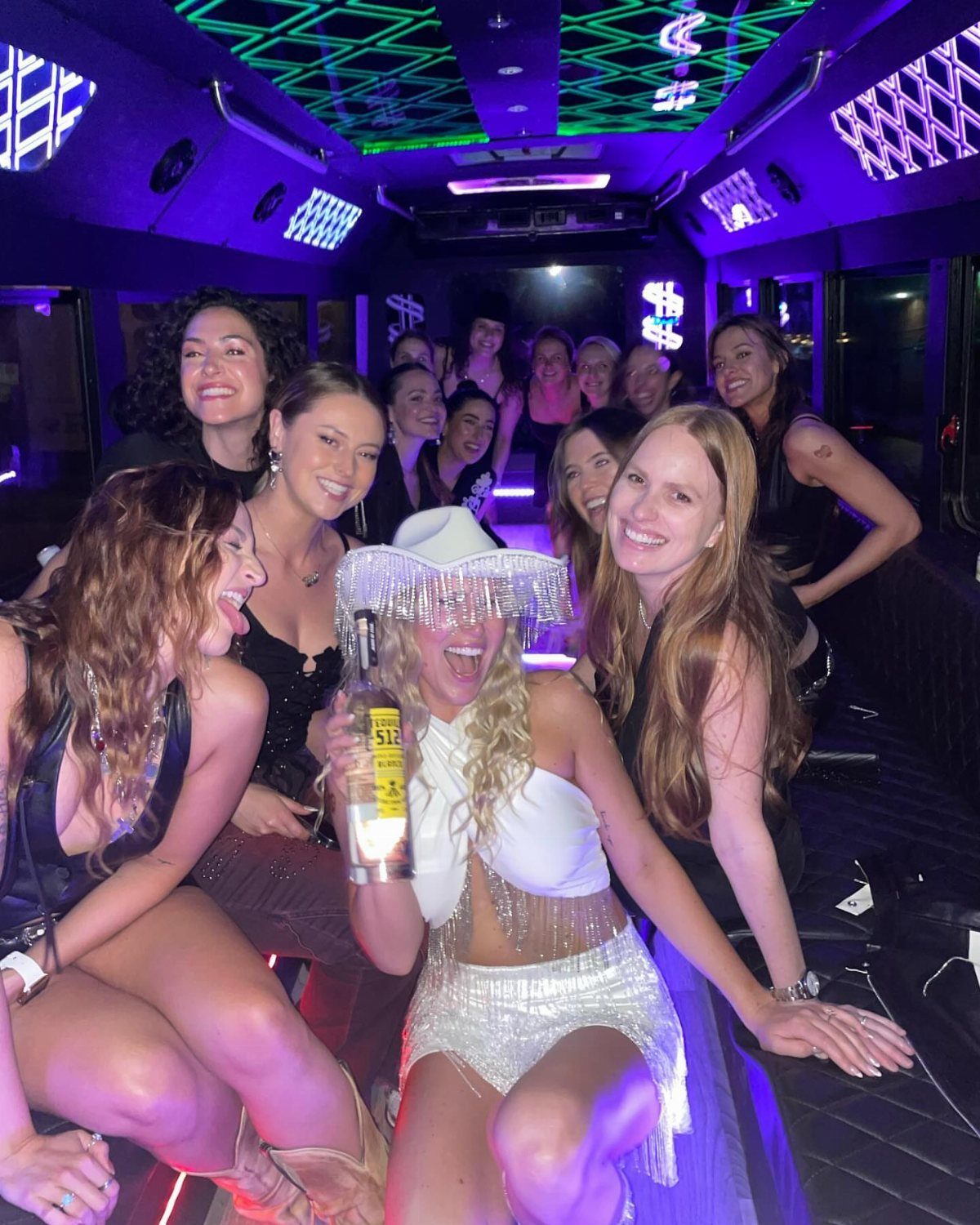 Group of young women smiling and posing inside a neon-lit party bus.