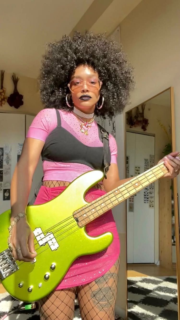 A person with a large black afro wig holding a lime green electric bass guitar.
