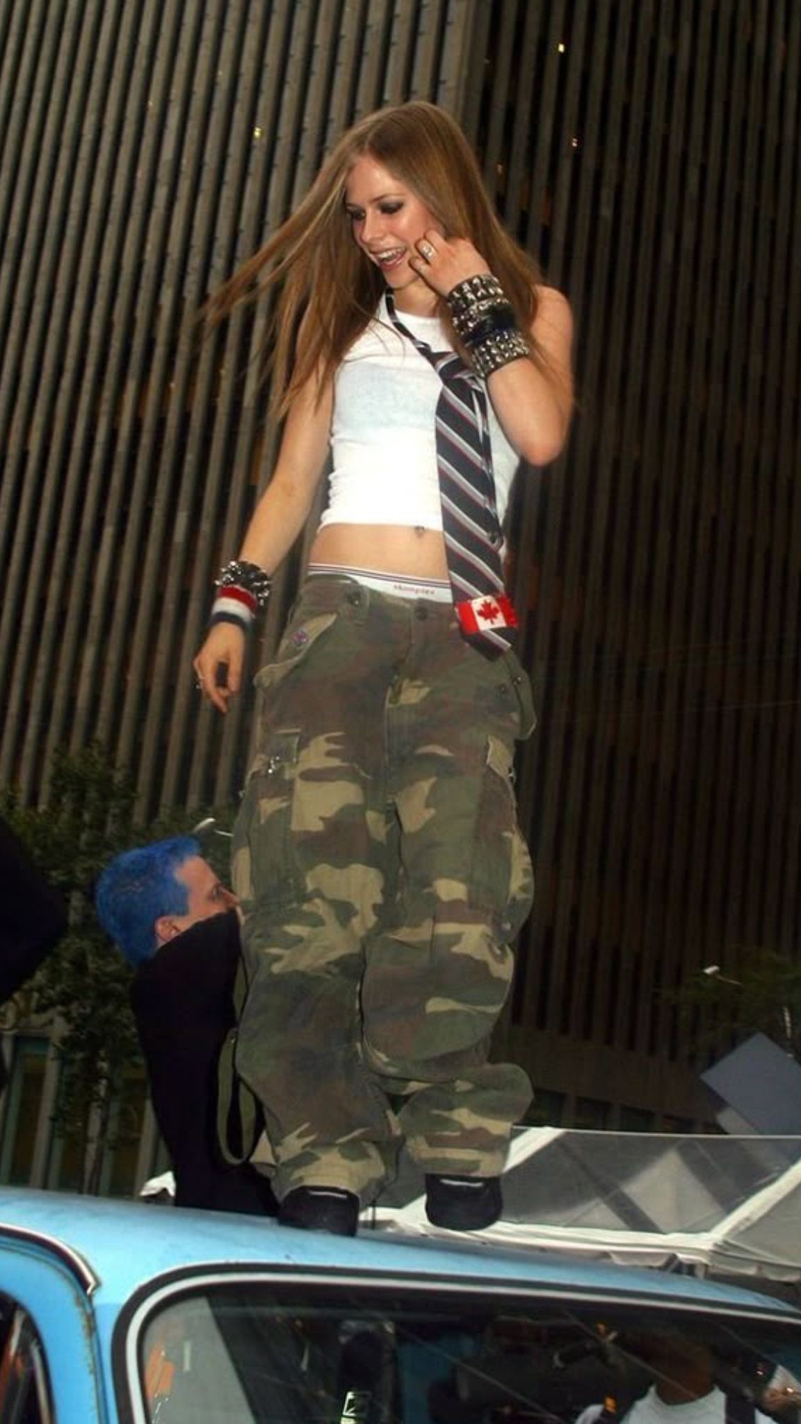 A woman wearing a white cropped tank top and camouflage cargo pants standing outdoors.
