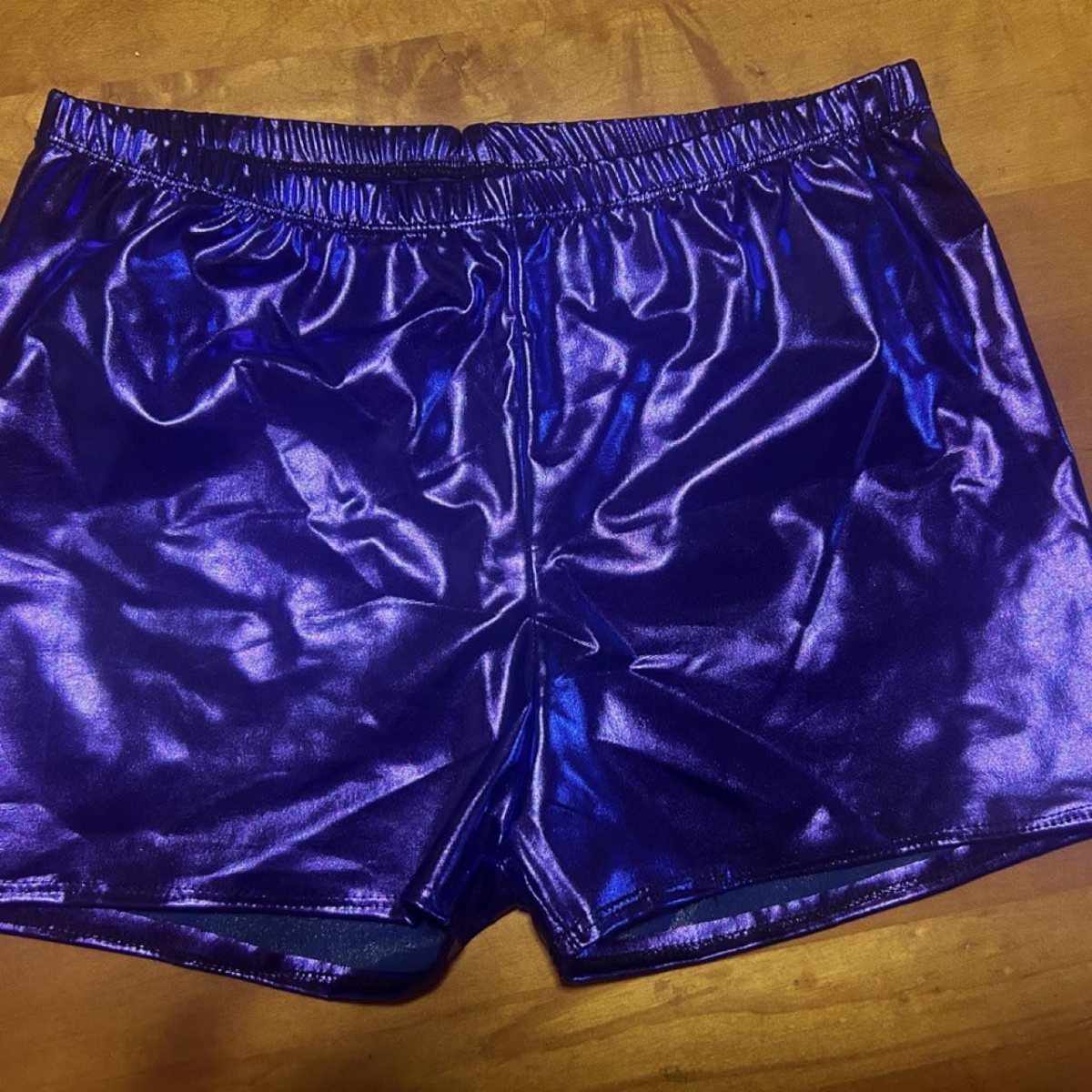 Metallic purple spandex shorts lying flat on a brown wooden surface.