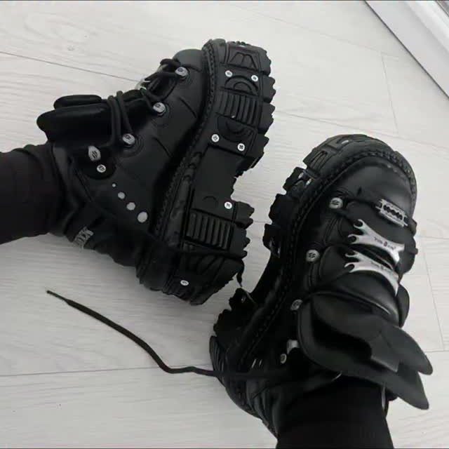 Black chunky platform combat boots with thick lugged soles on a light wooden floor.