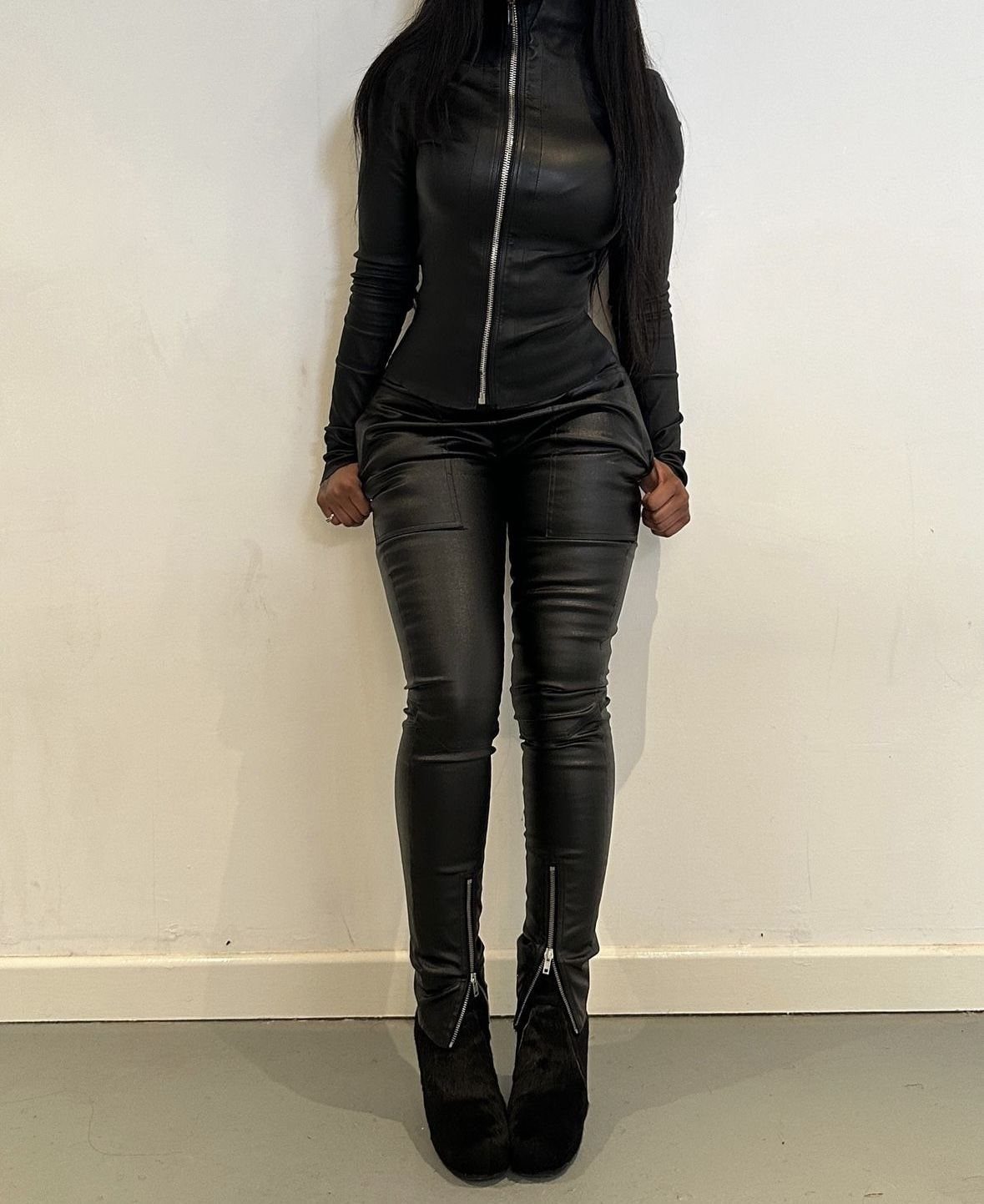 Person wearing black faux leather trousers and a matching zip-up top with platform boots.