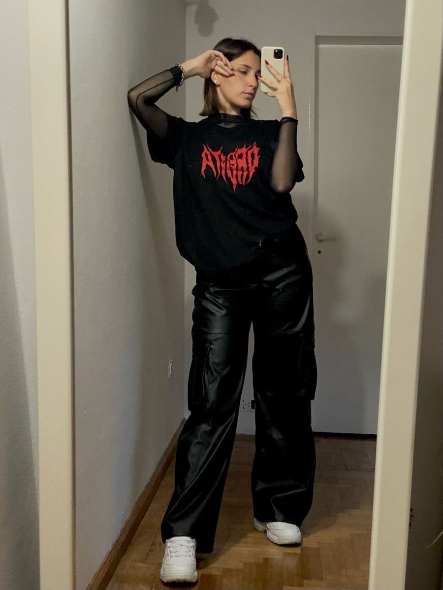 Woman in black graphic t-shirt and faux leather trousers posing for a mirror selfie.