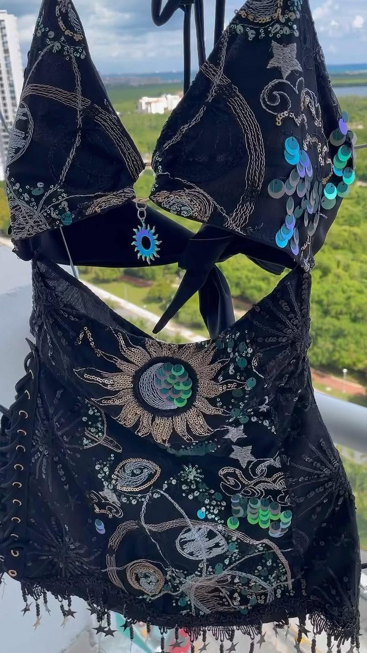 Black celestial embroidered rave outfit with silver patterns and teal sequins hanging outdoors.