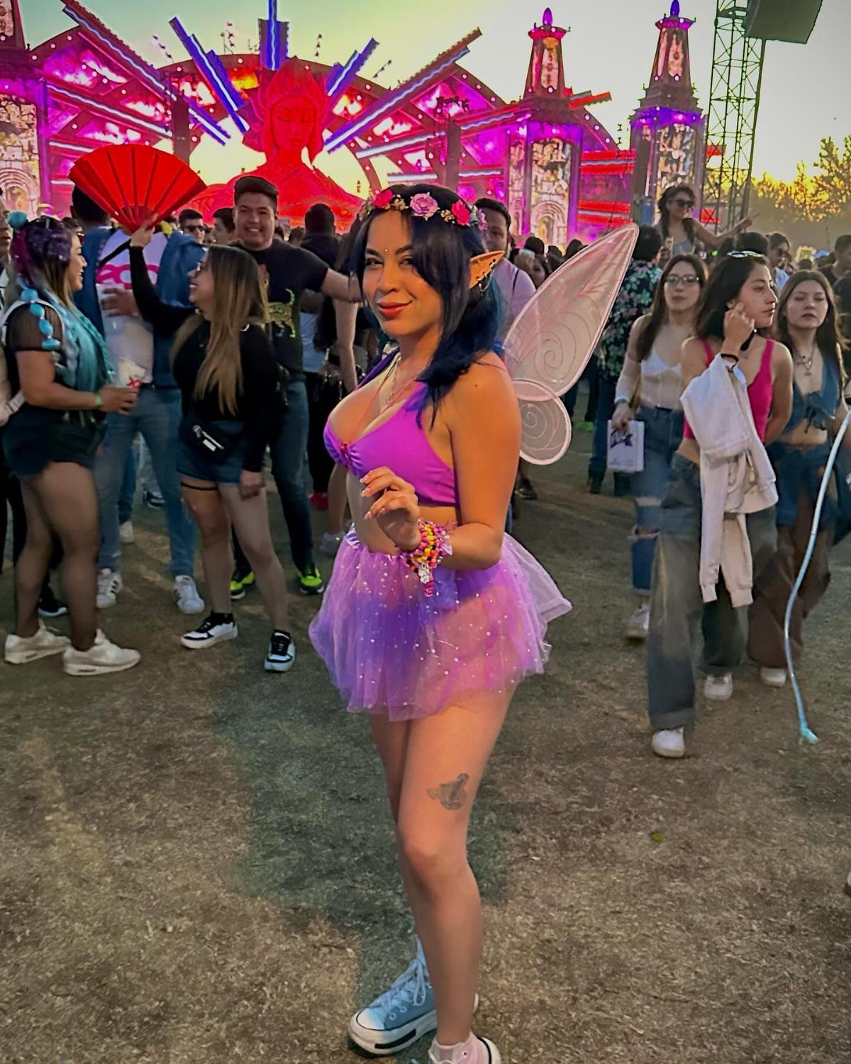 A woman wearing a purple fairy costume and wings at an outdoor music festival.