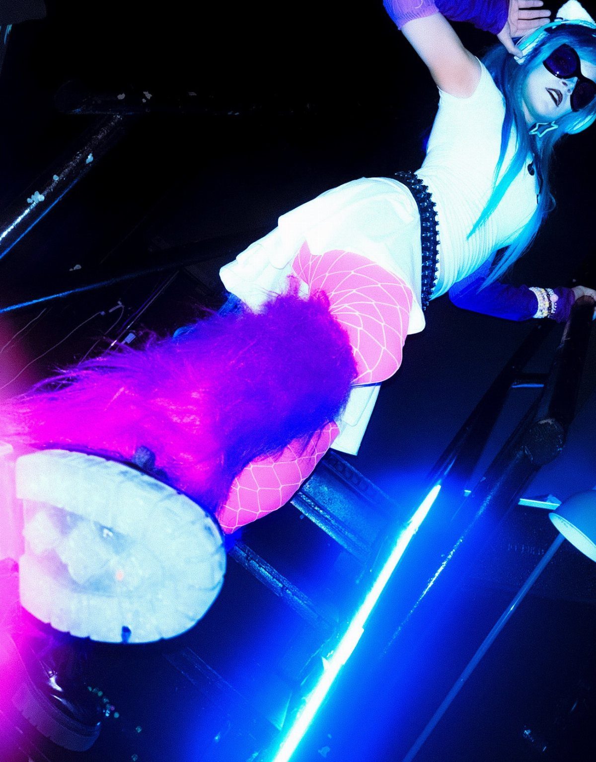 A person wearing a white dress, pink tights, and fuzzy pink leg warmers under blue lights.