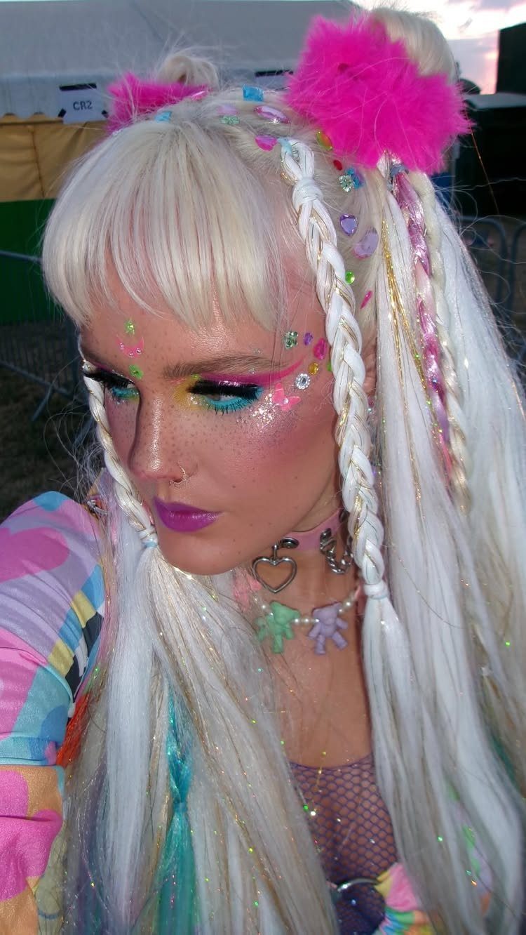 A person with blonde hair wearing colorful glitter makeup and pink hair accessories.