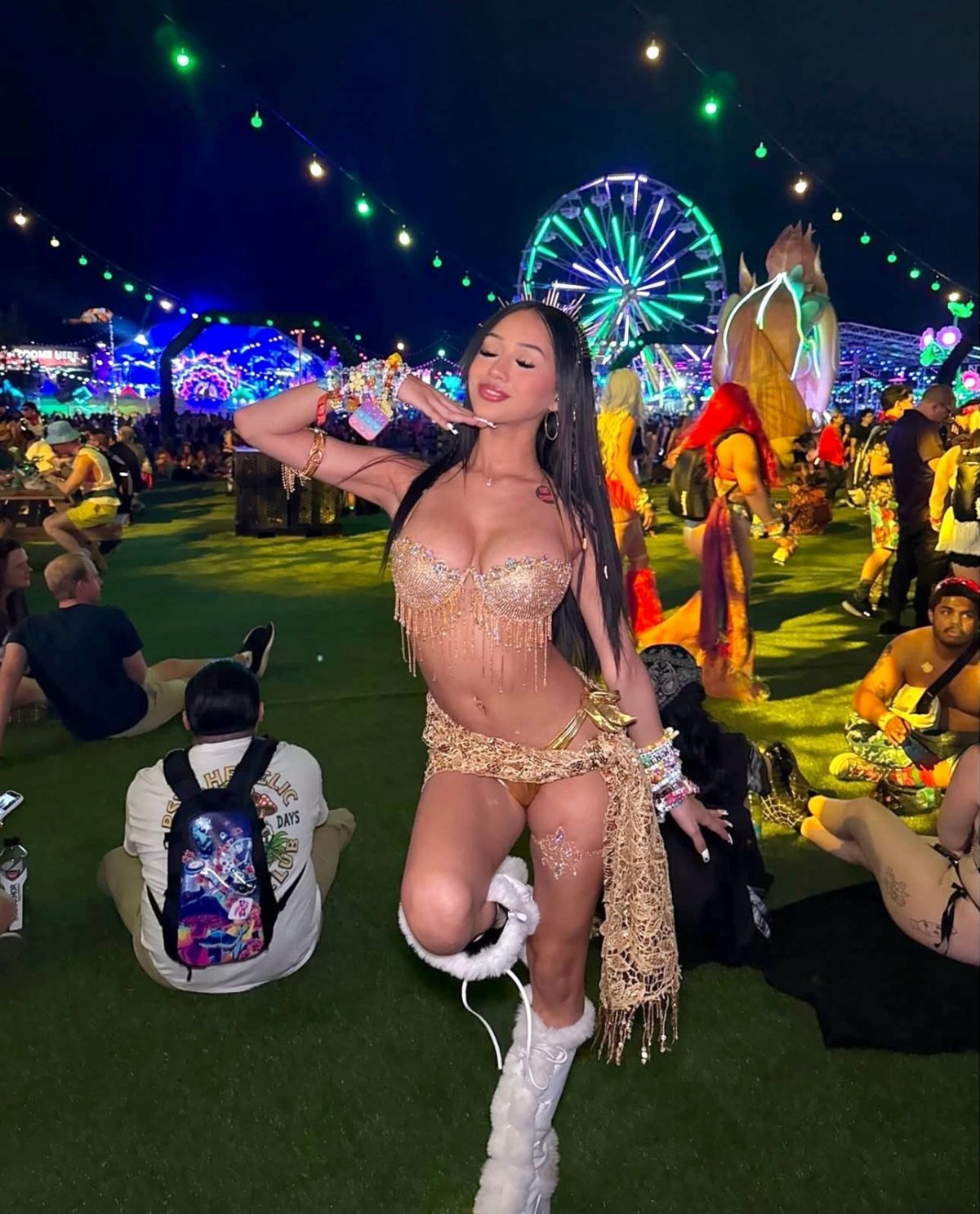 A woman posing in a gold sequined festival outfit with white platform boots at a night festival.