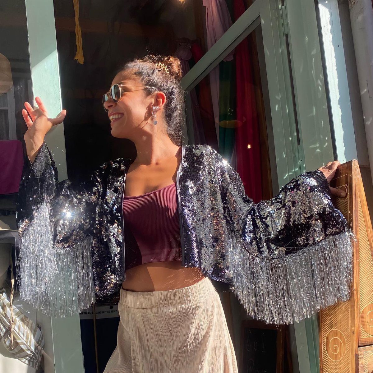 A woman smiling in a sequined black fringe jacket and maroon crop top.