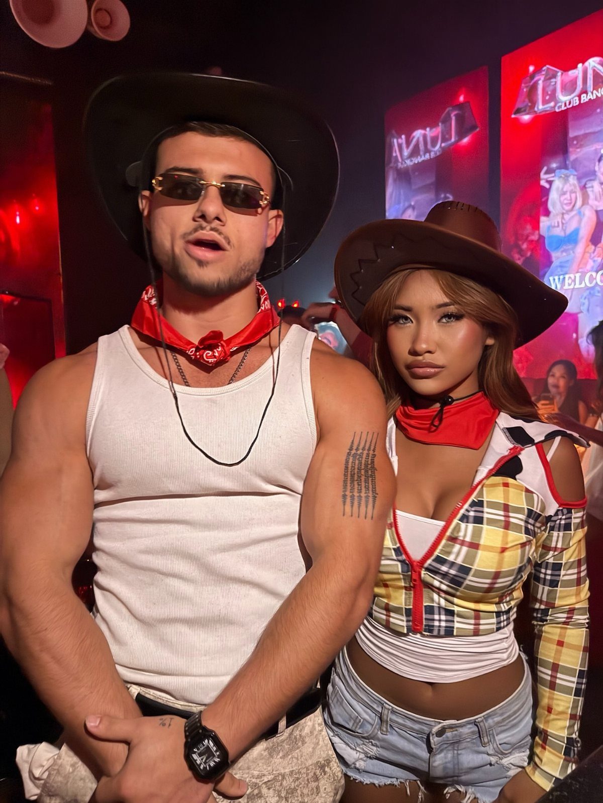 A man and woman posing in cowboy-themed club outfits with bandanas and hats.