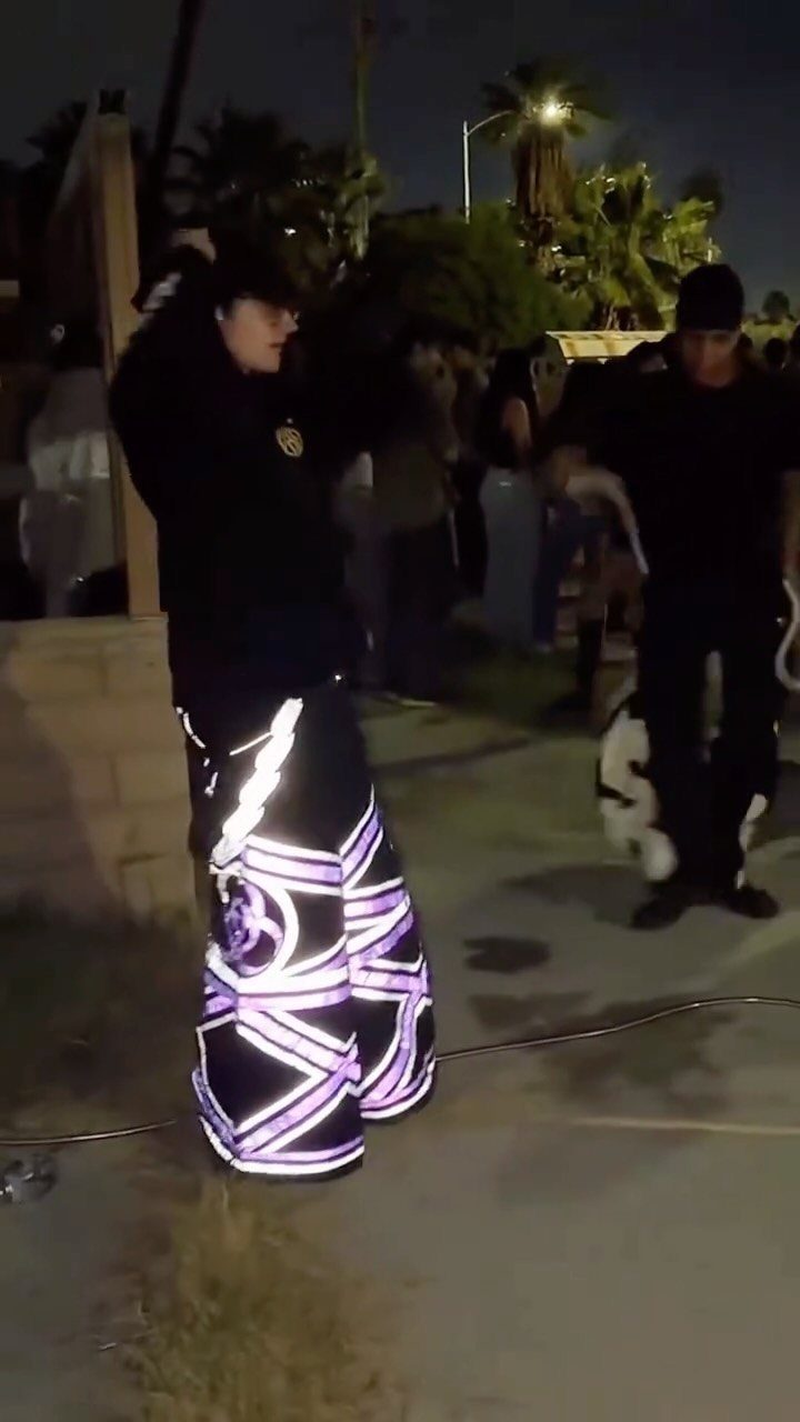 Person wearing black trousers with glowing purple neon patterns standing outdoors at night.