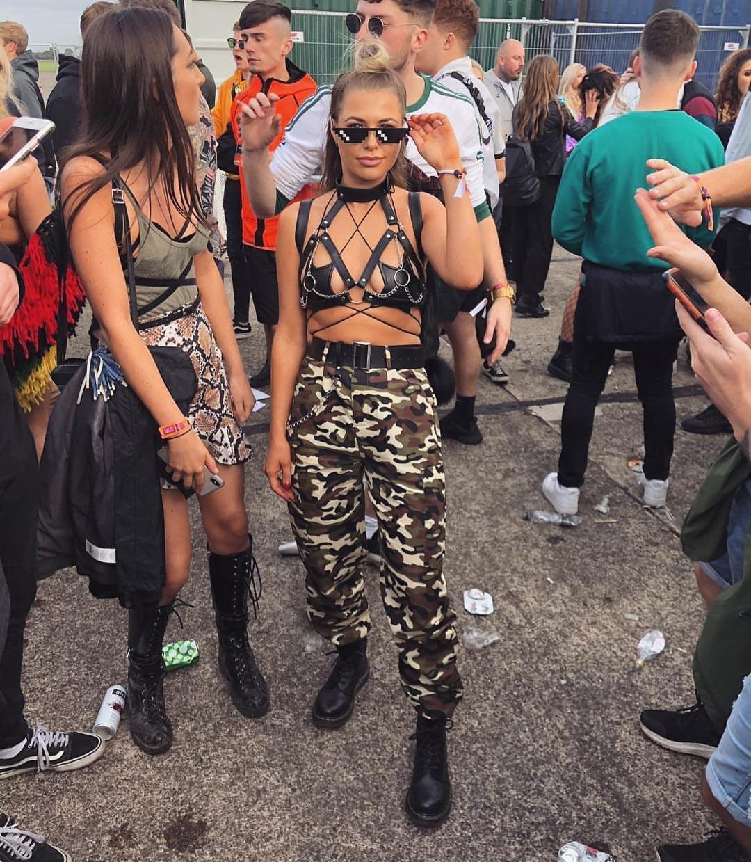Woman wearing a black harness top and camouflage pants standing in a crowded outdoor festival area.