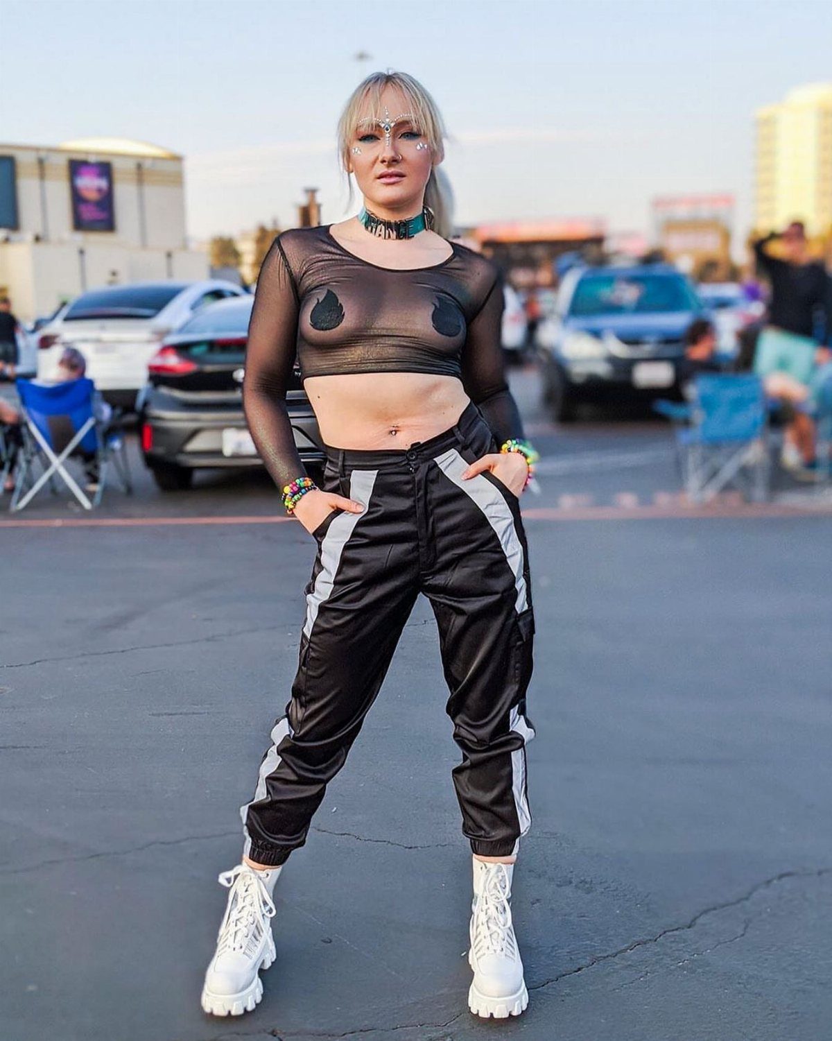 Woman posing in black mesh crop top, reflective cargo pants, and white platform boots.