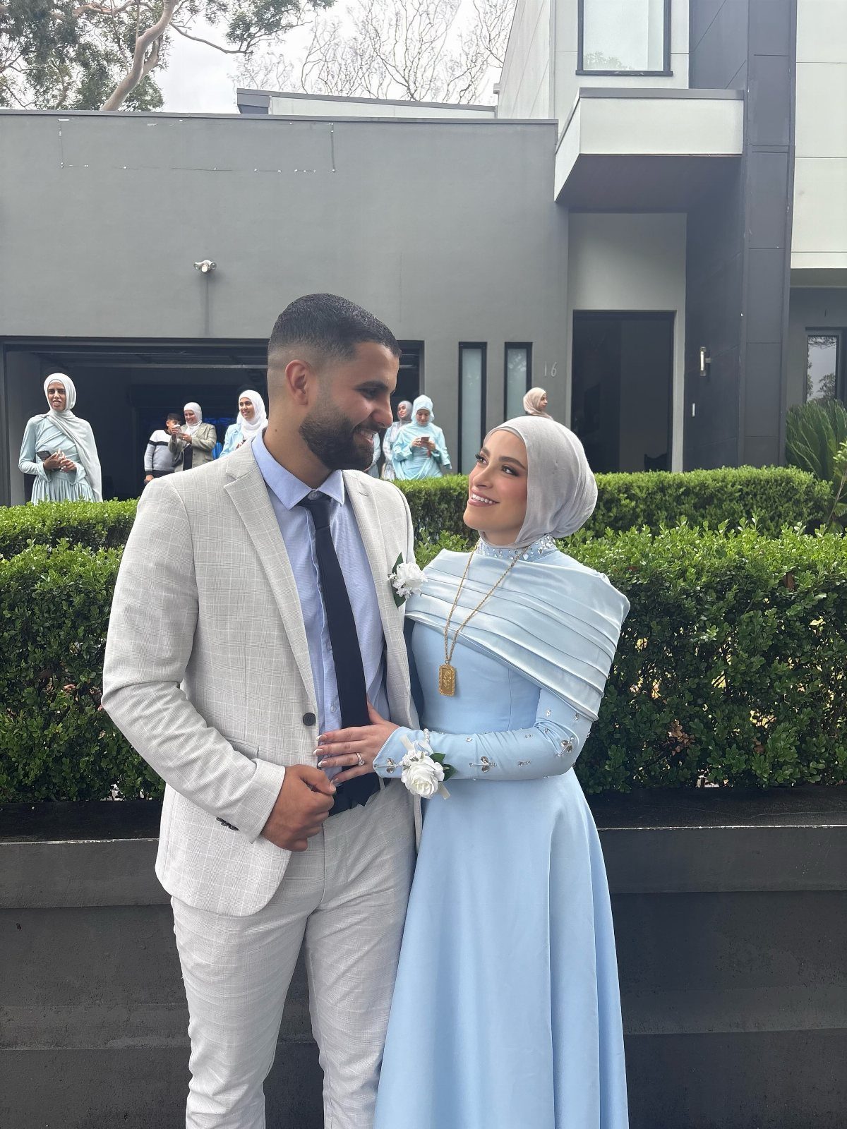A man in a white suit and a woman in a light blue dress smiling at each other.