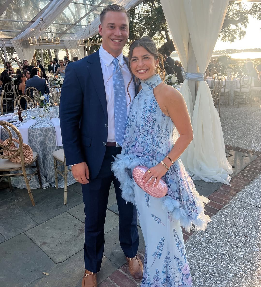 A man in a navy suit and a woman in a blue floral dress posing together.