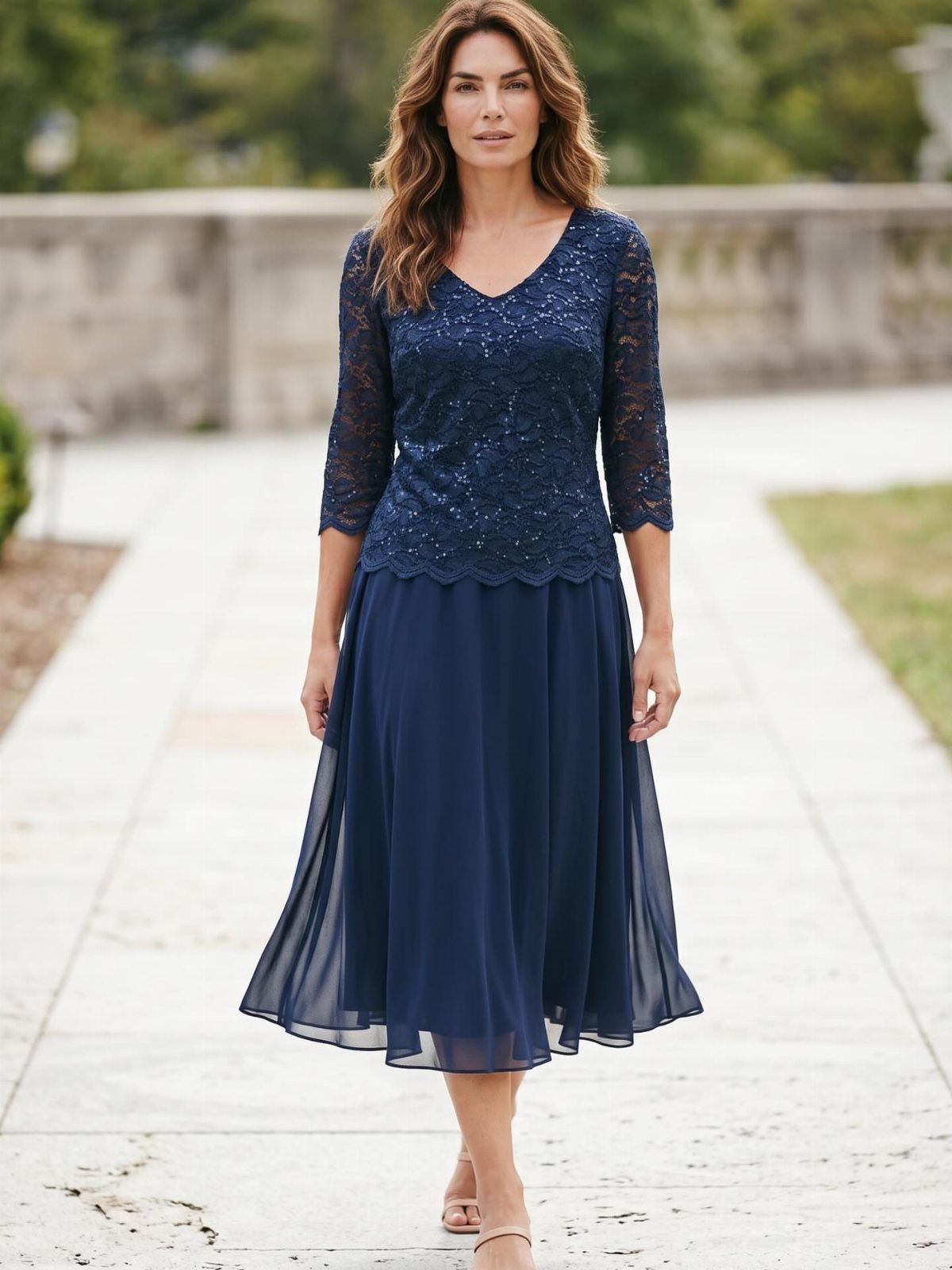 Woman walking outdoors wearing a navy blue glitter lace layered midi dress.