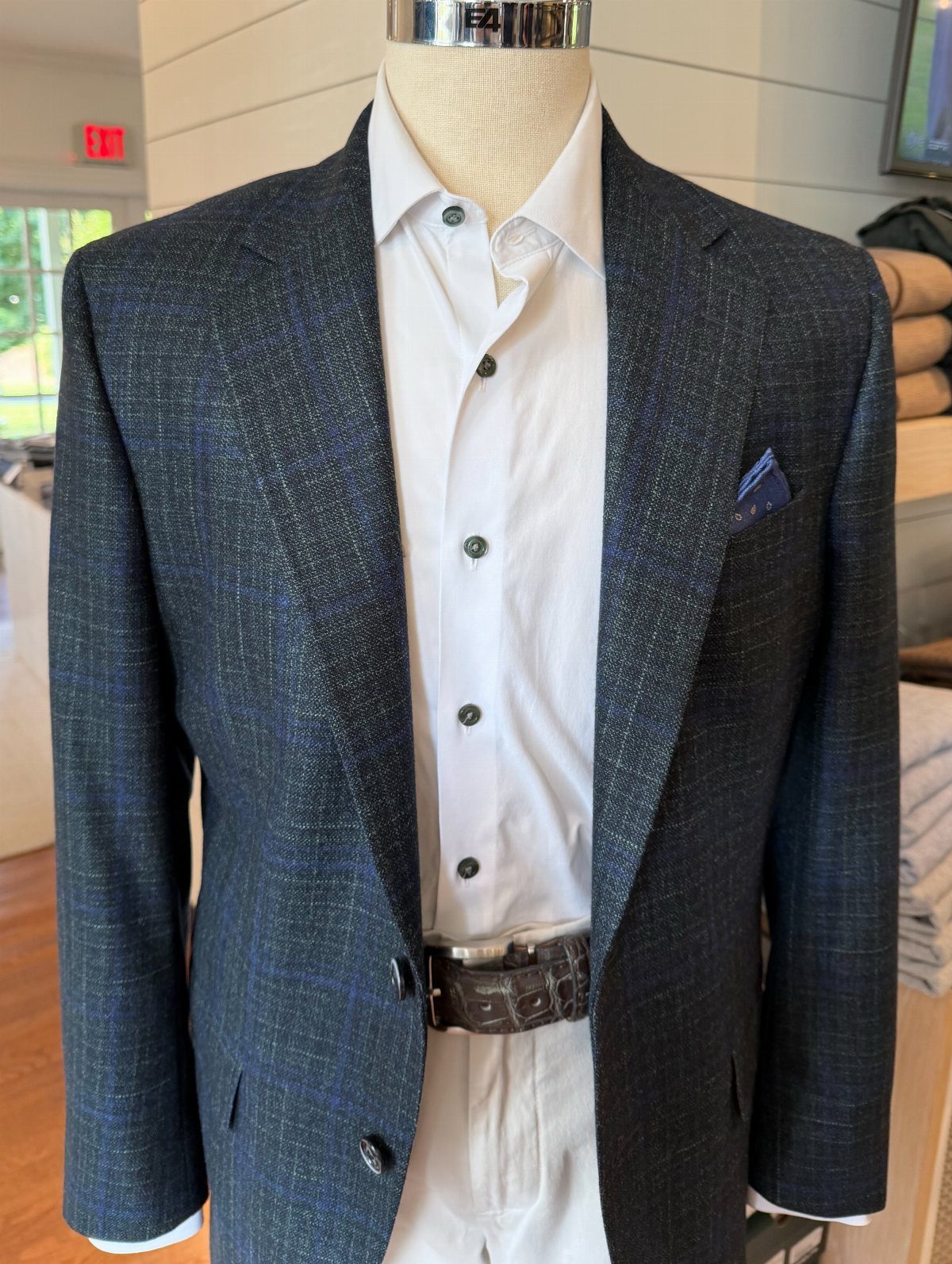 A mannequin dressed in a dark blue textured blazer, white shirt, and white trousers.