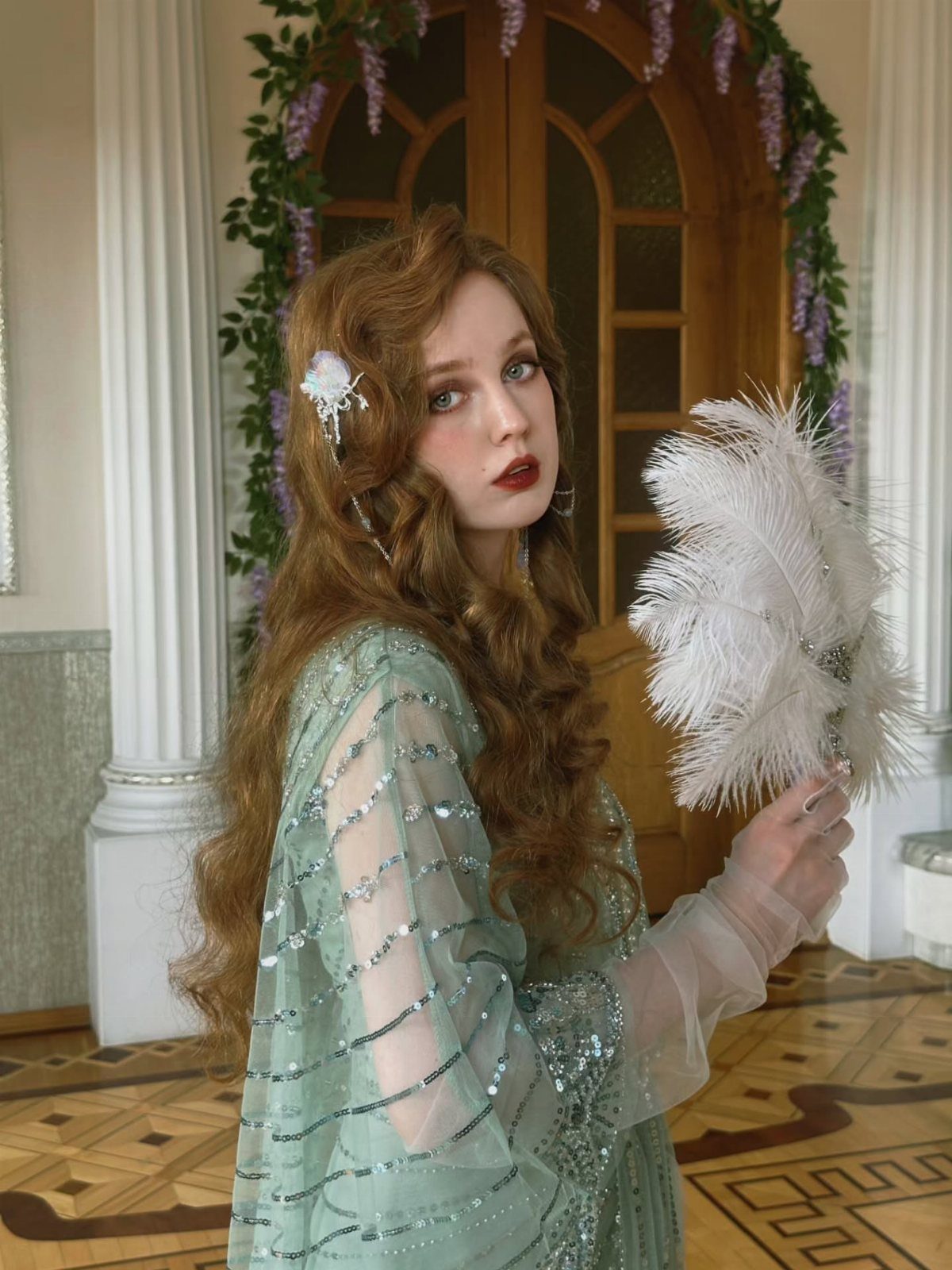 A woman in a mint green sequined dress holding a white feather fan.