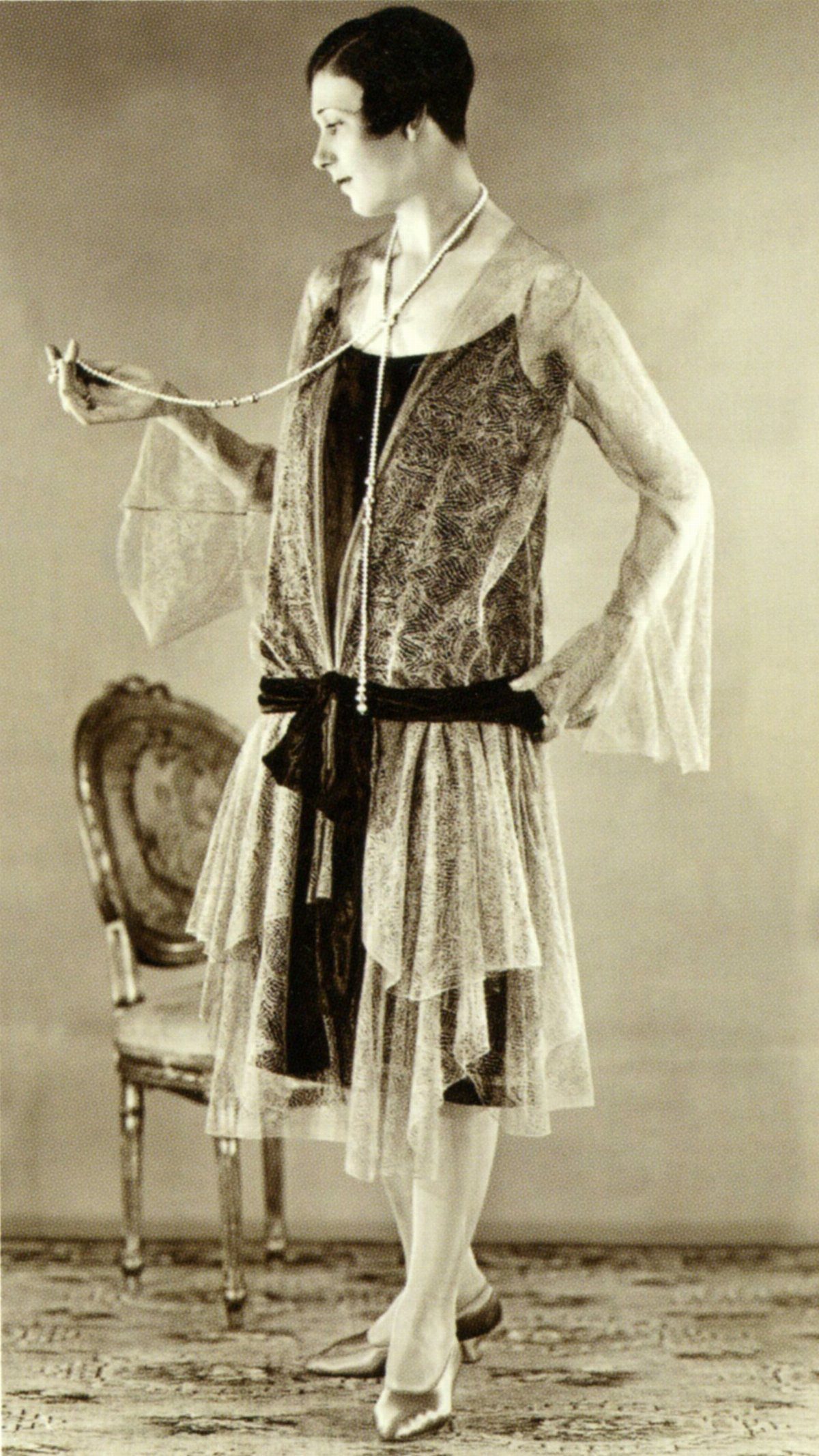 A woman posing in a vintage 1920s dress with a delicate lace overlay and long sleeves.