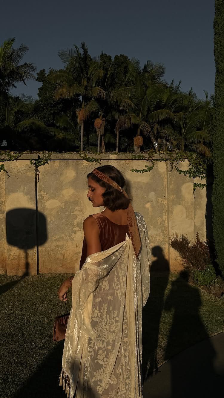 Woman in vintage attire wearing a patterned lace shawl standing outdoors near palm trees.