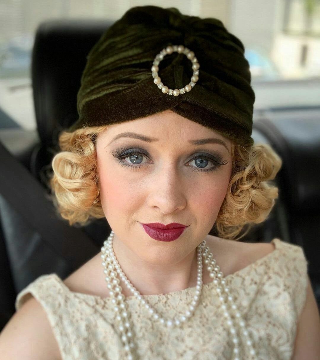 Woman wearing a dark green velvet turban with a pearl circular ornament and pearl necklaces.