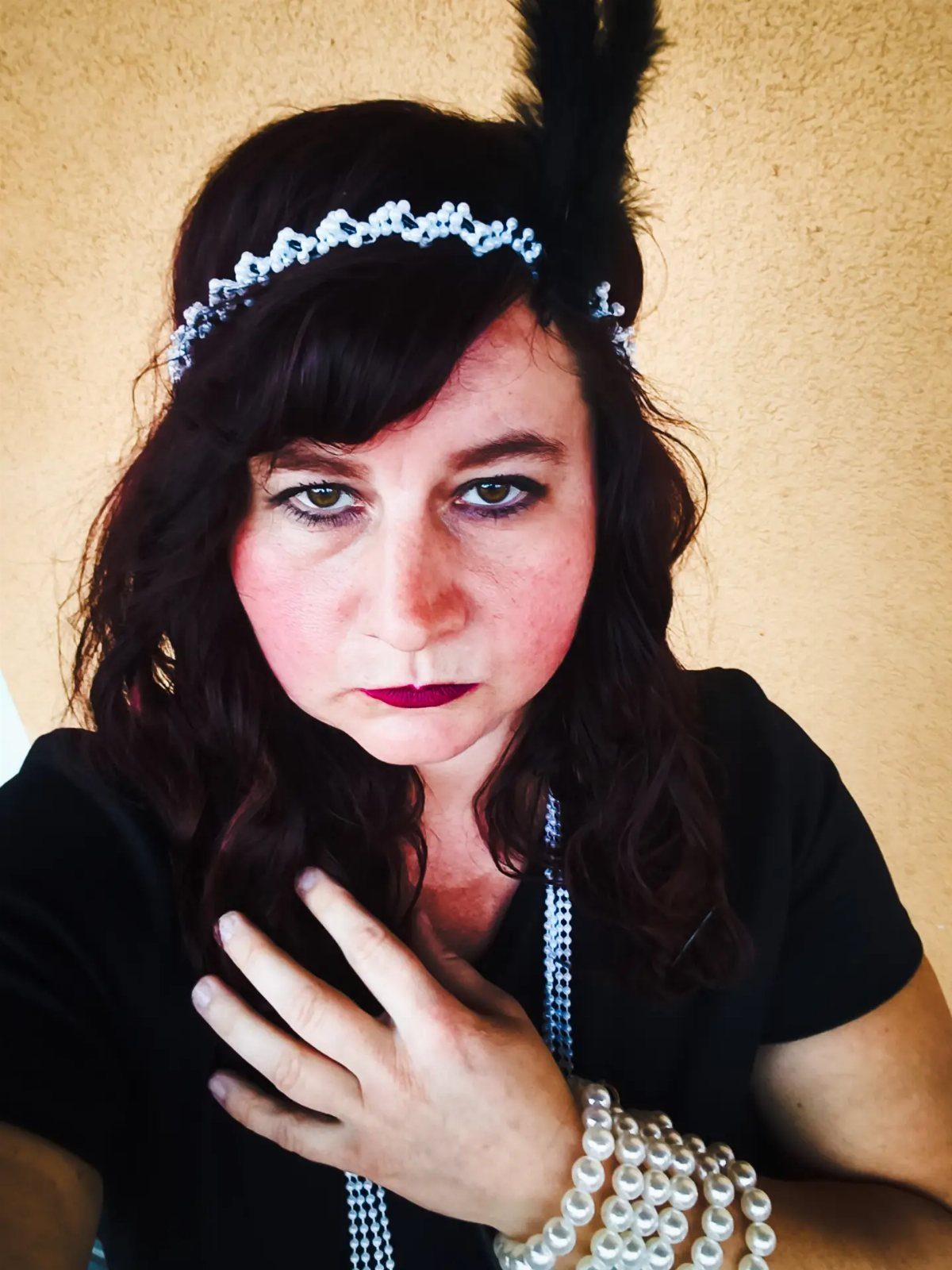 Woman wearing a beaded headband with a black feather and pearl jewelry.