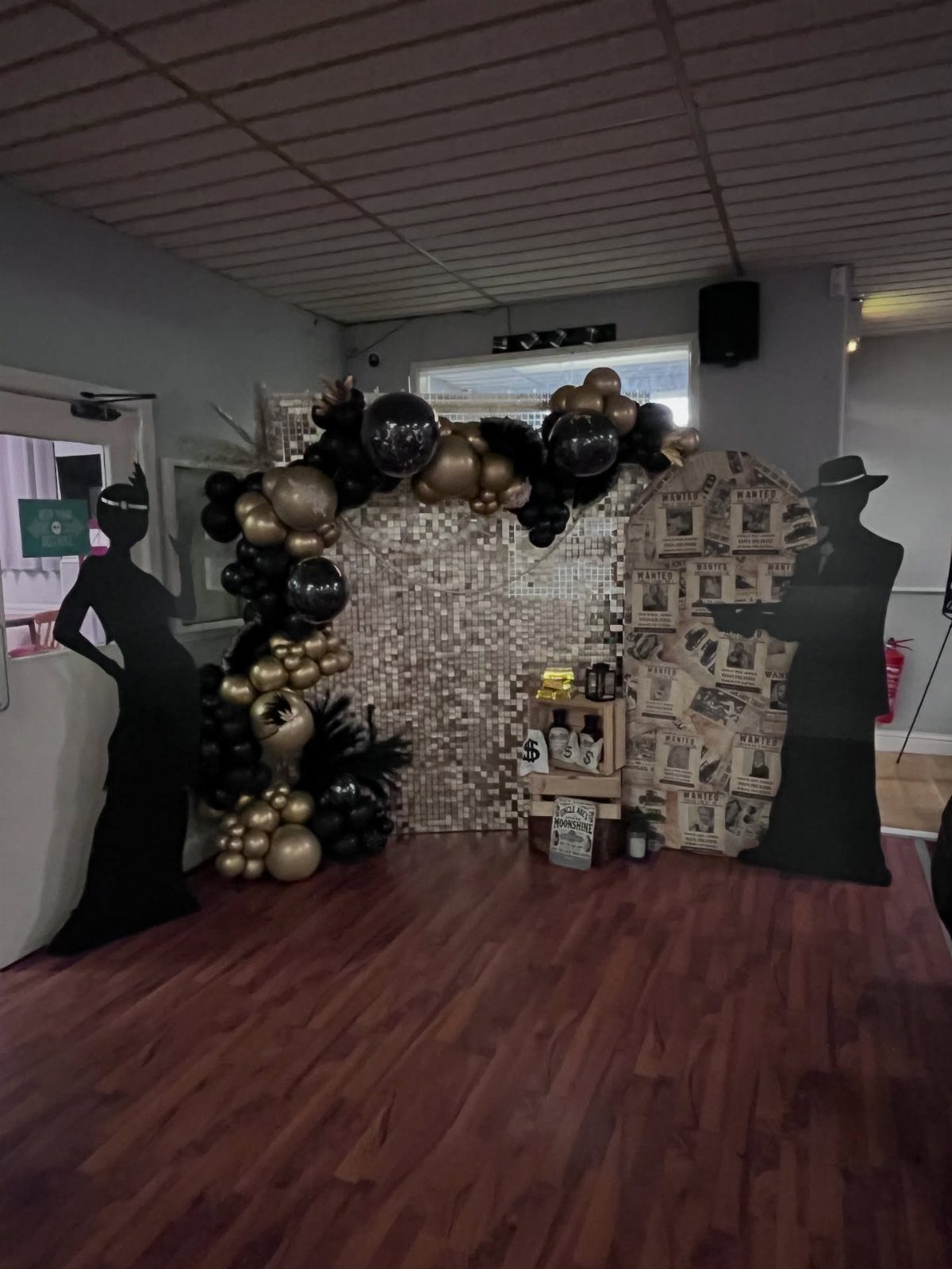 Black and gold balloon arch surrounding a sequin backdrop with themed cardboard silhouettes.
