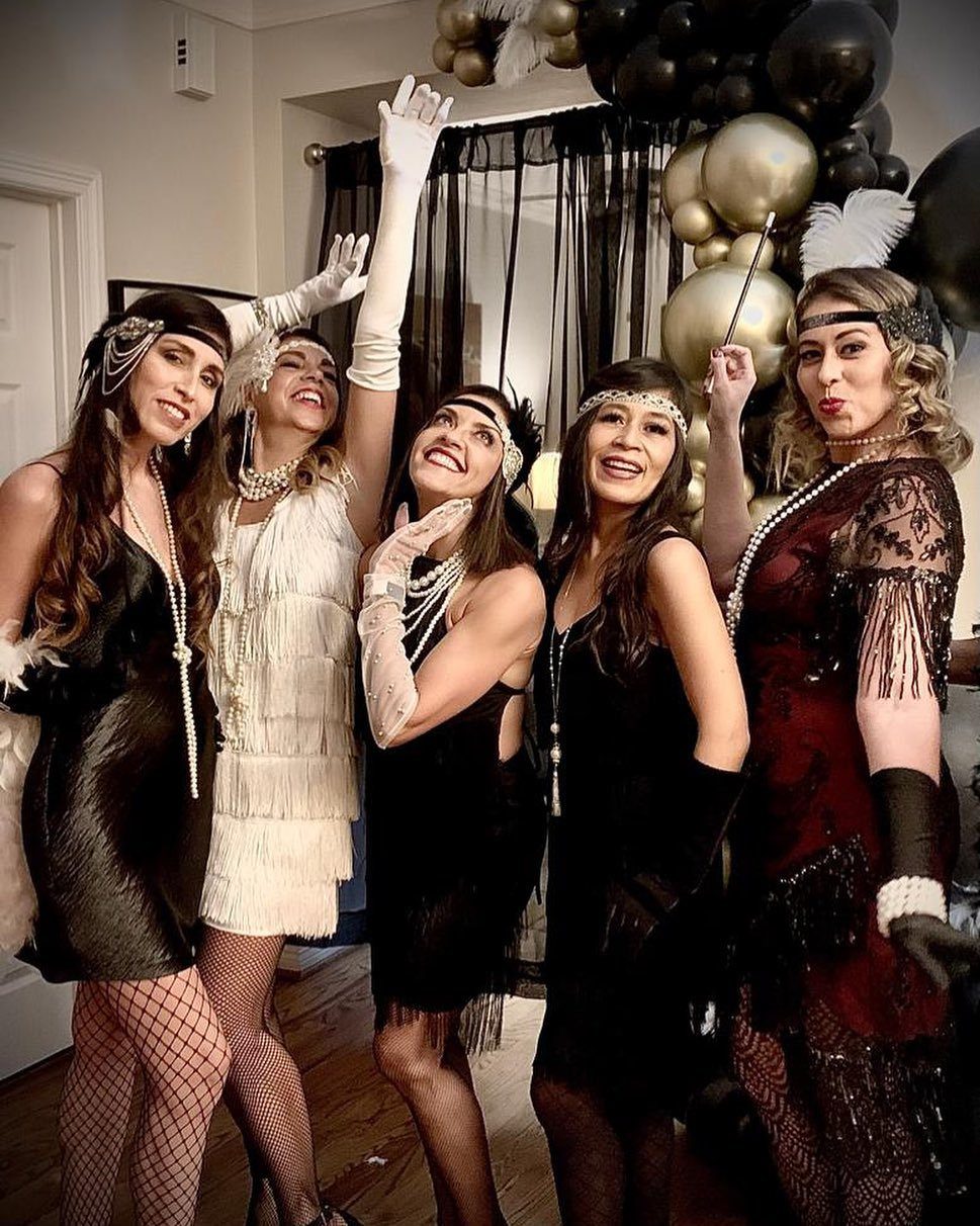 Five women dressed in 1920s flapper fashion posing together for a celebratory photo.