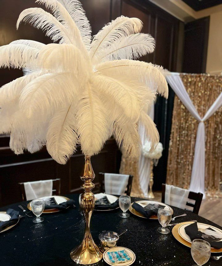 White ostrich feather centerpiece on a gold stand atop a formal black banquet table.