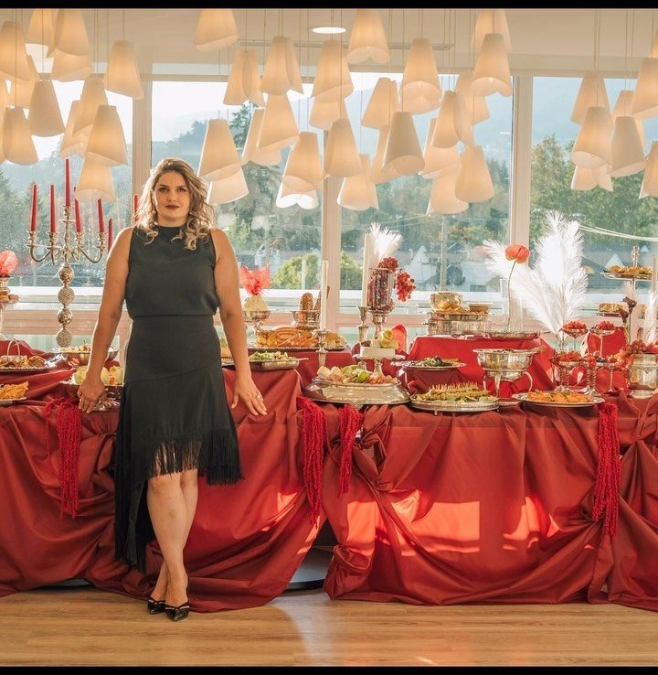 Woman in a black fringe dress standing by a large red buffet table filled with food.