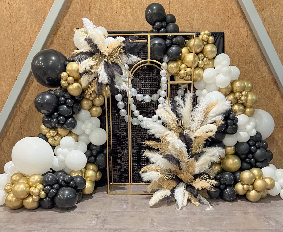 Gold, black, and white balloon arch with pampas grass decorating a gold frame.