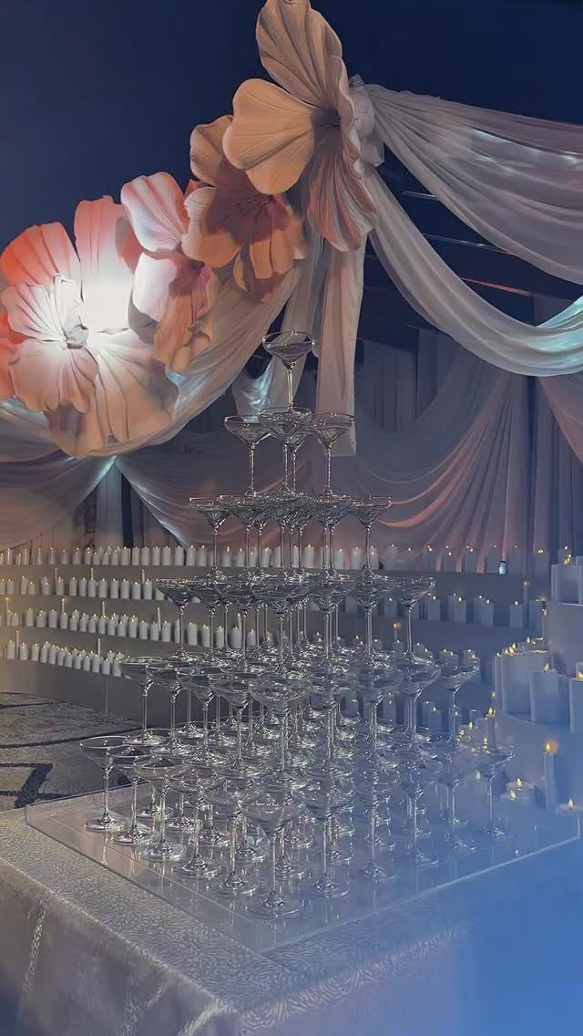 A large pyramid of coupe glasses arranged as a champagne tower in a dimly lit room.