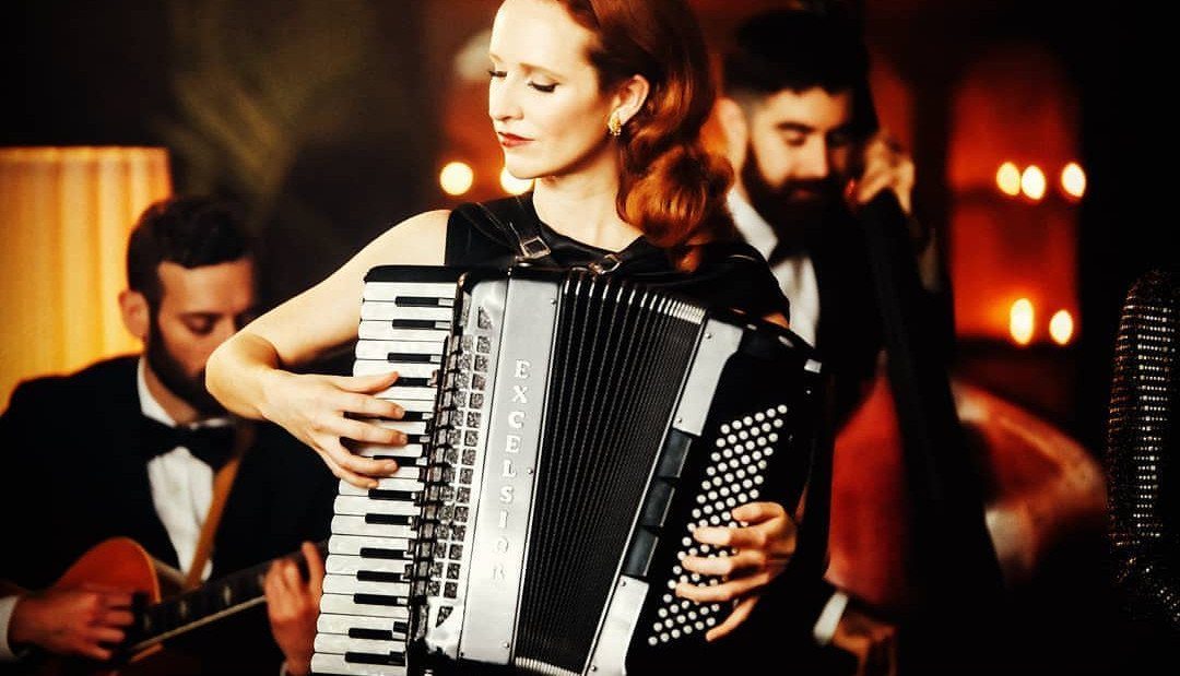 A woman playing an accordion while musicians play guitar and double bass in a dim setting.