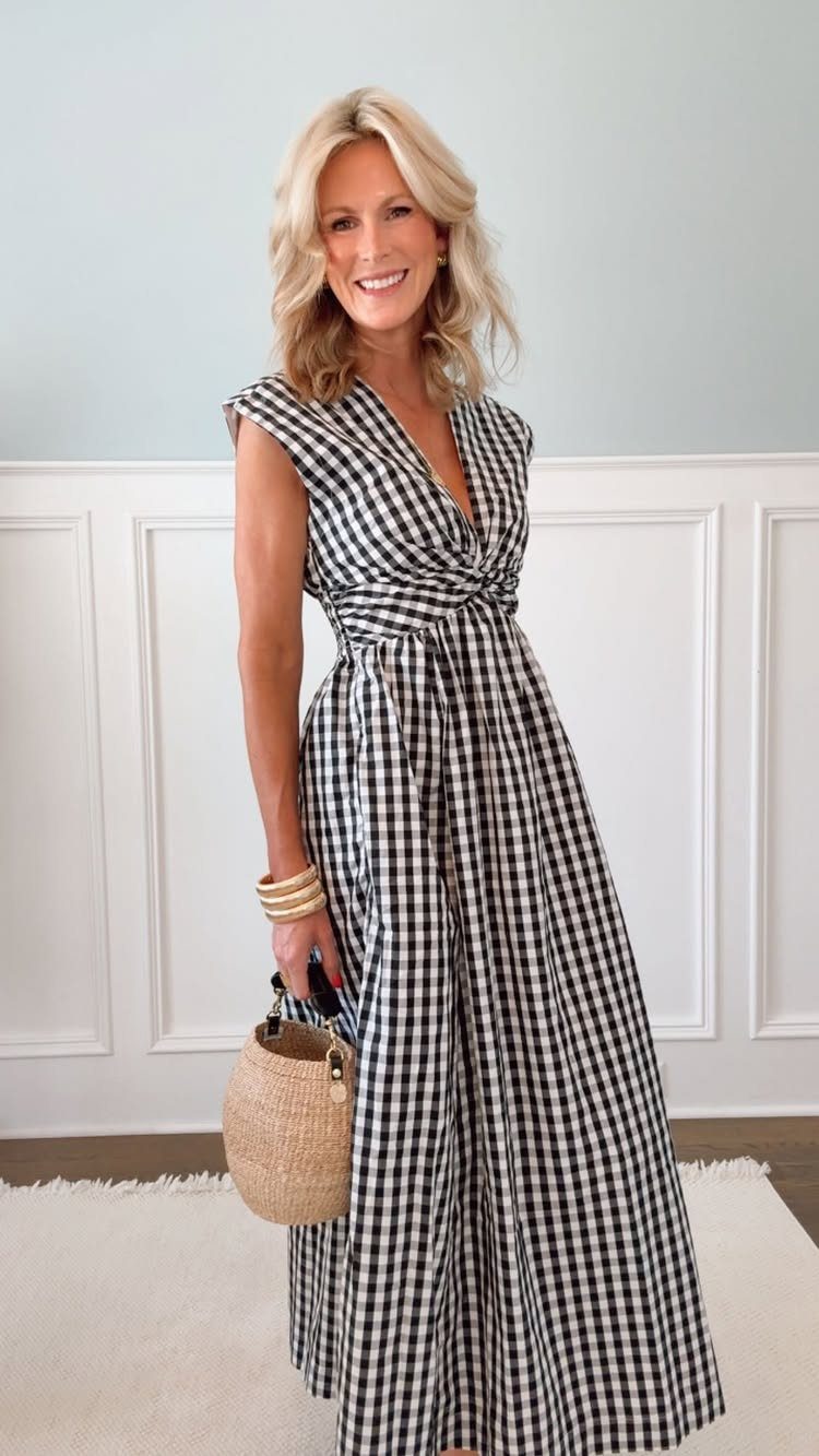 A blonde woman posing in a black and white gingham maxi dress holding a straw bag.