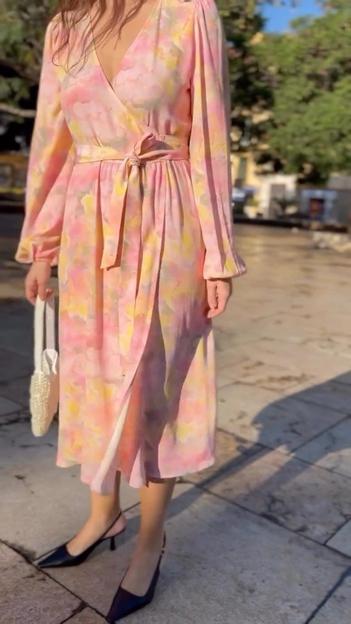 A person wearing a pastel floral wrap dress and black kitten heels standing outdoors.