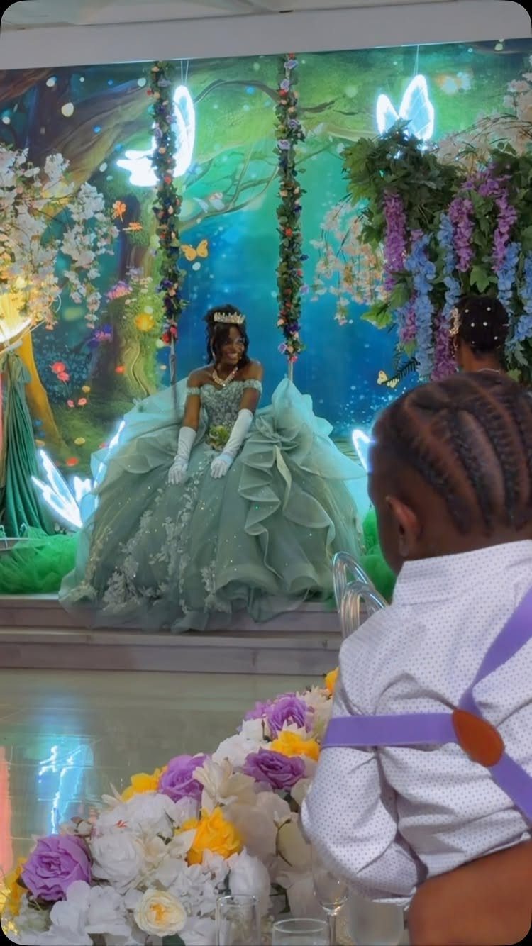A girl in a mint green ball gown sits within a magical forest-themed display.