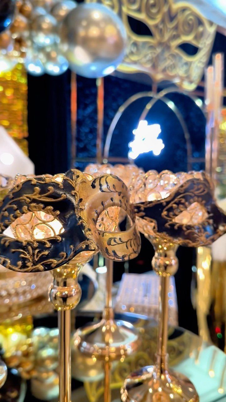 Ornate black and gold masquerade masks displayed on elegant gold stands against a shimmering background.