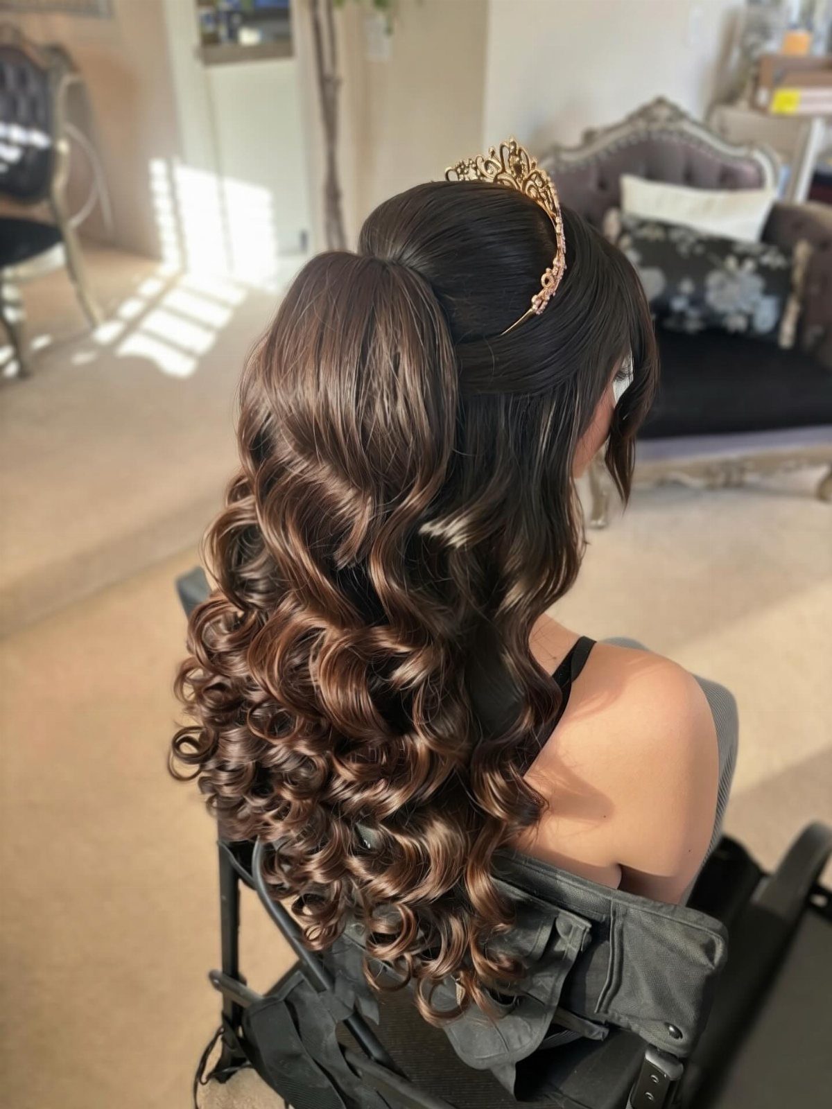 Long dark brown hair styled in voluminous glossy curls with a gold jeweled tiara.